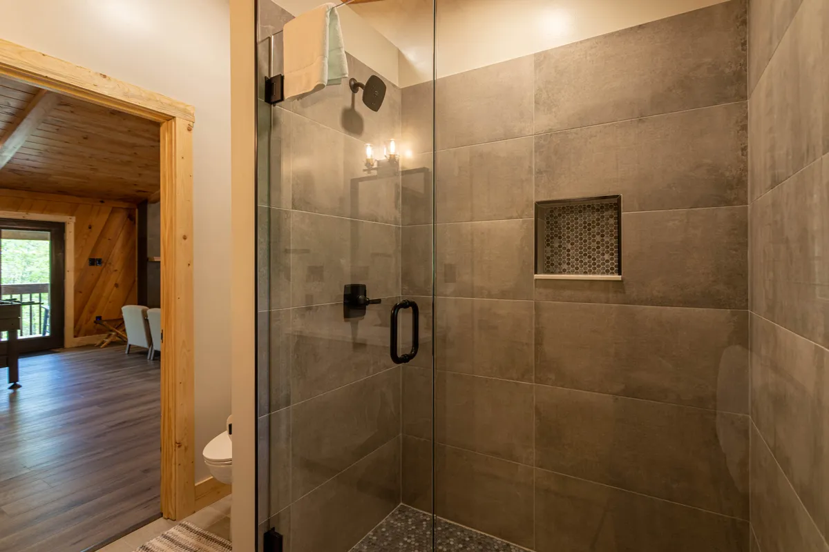 A modern bathroom with a glass shower enclosure, textured tile walls, and a decorative shower niche. The space exudes a spa-like feel, offering a refreshing and rejuvenating environment after a day outdoors.