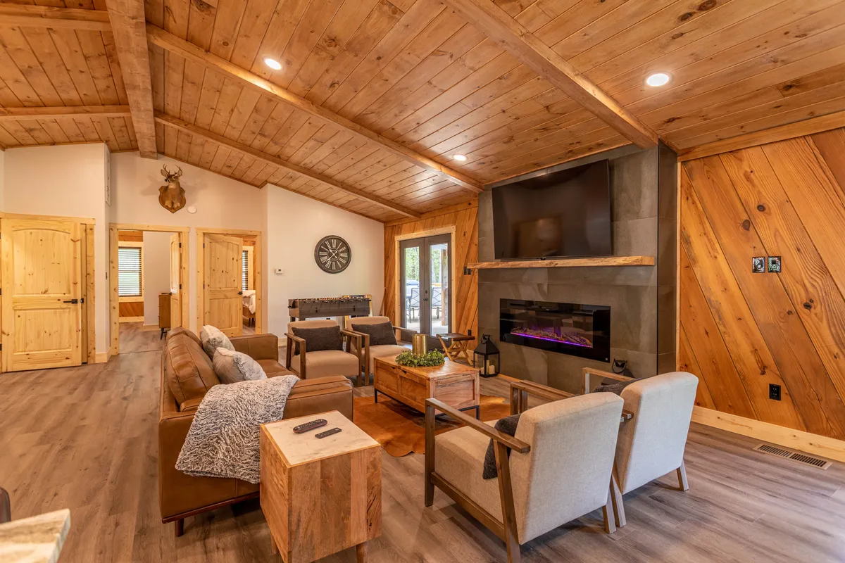 A cozy interior living area with a crackling fireplace, a vaulted wooden ceiling, and a comfortable seating arrangement ideal for socializing, reading, or watching TV. The warm ambiance is ideal for gatherings or quiet evenings inside.
