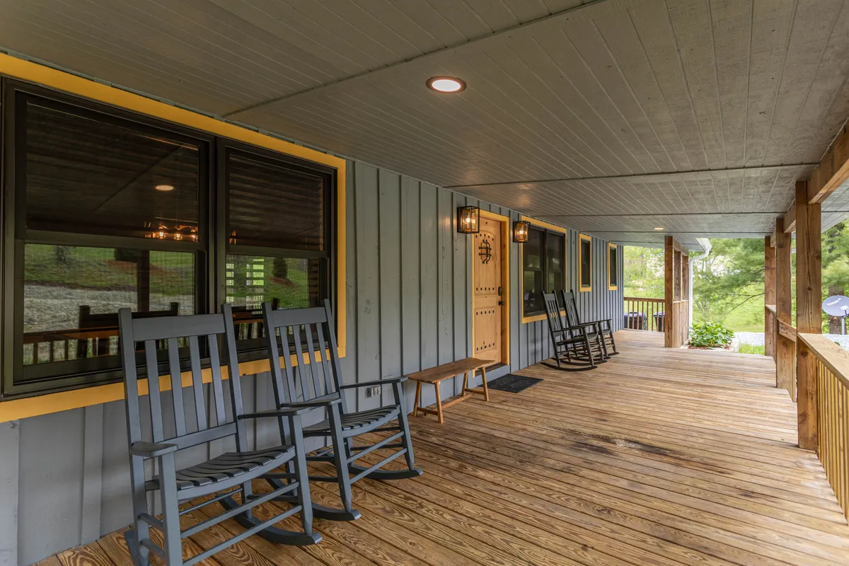 Front porch scene featuring classic rocking chairs, a welcoming front door, and large windows—set against a backdrop of wooded serenity. The arrangement suggests a spot for evening chats, morning coffee, or simply soaking in the peaceful environment.