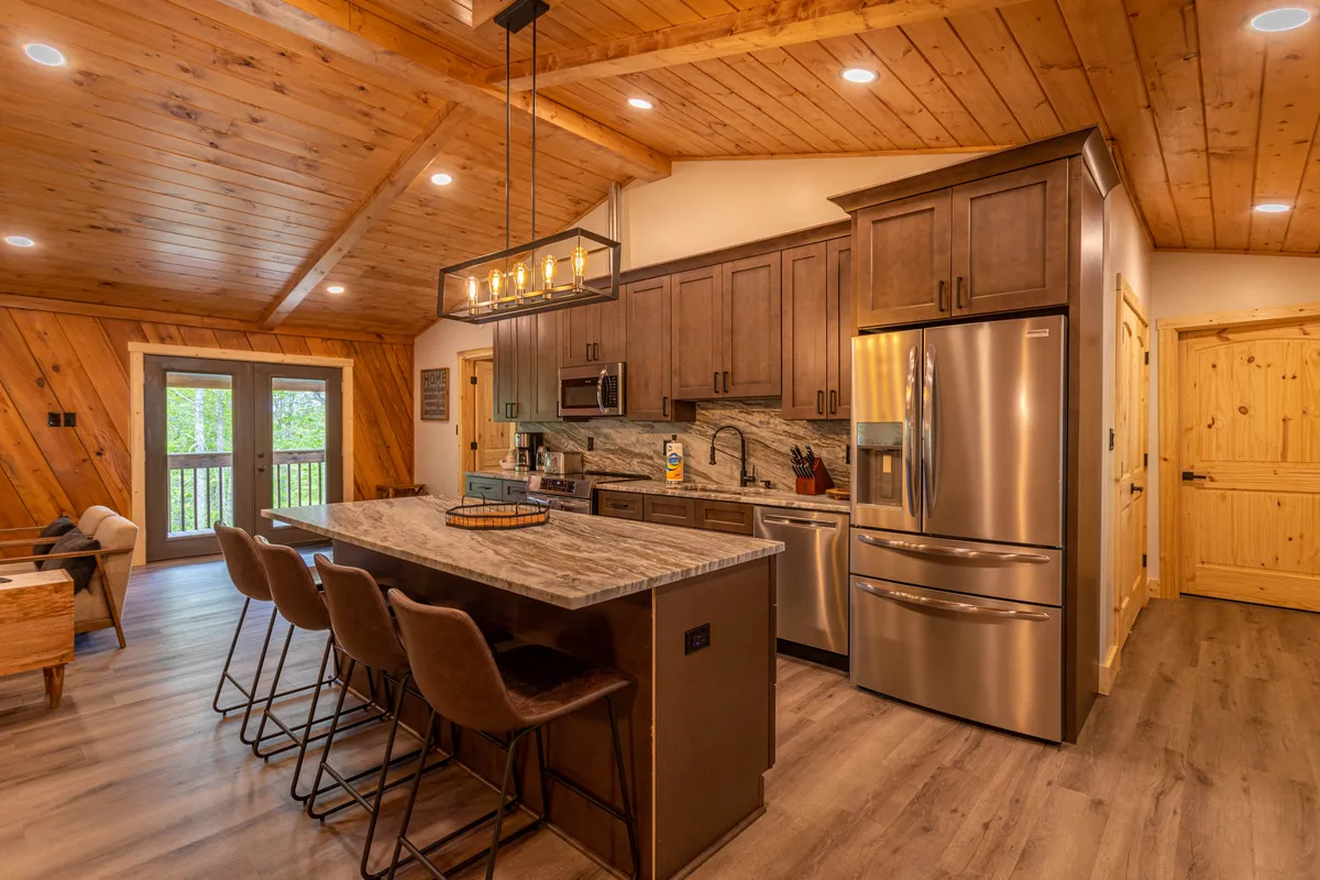 A close look at the remodeled kitchen with a large granite island, seating for four, stainless steel appliances, and a warm wooden ceiling. Bright lighting and modern finishes make this kitchen inviting and functional for preparing meals and socializing.