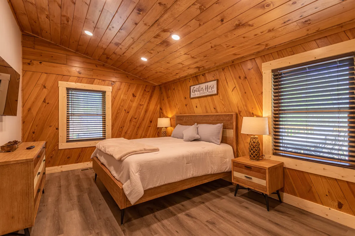 A serene bedroom with light bedding, wooden wall panels, decorative lamps, and a nightstand, bathed in natural light. The tidy and uncluttered design conveys a sense of calm and a hypoallergenic environment.