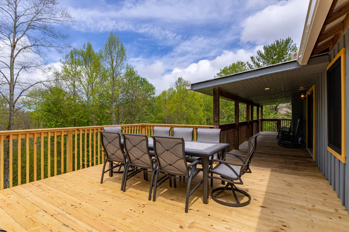 A cozy outdoor dining setup on a spacious deck surrounded by greenery, with a sturdy table set for meals and views of the trees beyond. The deck’s railing frames the scene, suggesting a safe, communal space for families to relax and dine together in the open air.